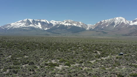 Wide-shot-of-the-Sierra-Nevada-mountains-with-a-car-standing-in-the-desert-landscape