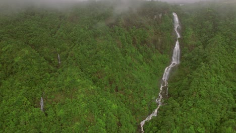 A-misty-and-cloudy-aerial-perspective-captures-a-multi-tiered-waterfall-amidst-the-humid-atmosphere-of-Sa-Pa-in-Vietnam's-Hoàng-Liên-Son-Mountains,-where-it-gracefully-cascades-over-rocky-cliffs