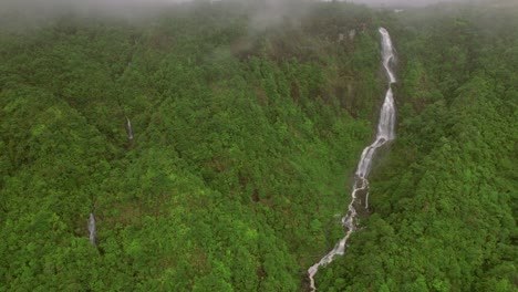 Una-Perspectiva-Aérea-Brumosa-Y-Nublada-Captura-Una-Cascada-De-Varios-Niveles-En-Medio-De-La-Atmósfera-Húmeda-De-Sa-Pa-En-Las-Montañas-Hoàng-Liên-Son-De-Vietnam,-Donde-Cae-Con-Gracia-Sobre-Acantilados-Rocosos.