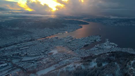 Golden-hour-light-breaks-between-dense-clouds-in-Bergen-Norway-snow-covered-city