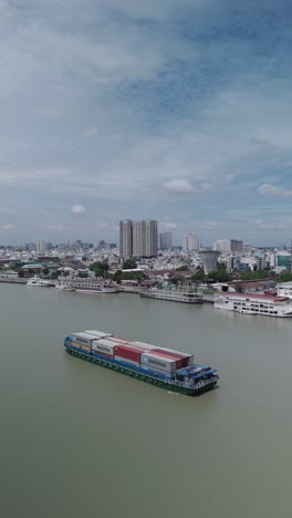 Saigon-River-container-barge-on-sunny-day-with-Ho-Chi-Minh-City-in-high-res-vertical-video