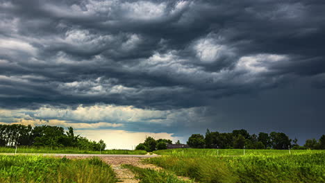 A-mesmerizing-time-lapse-of-storm-clouds-gathering-over-a-rural-landscape,-with-a-country-road-passing-past-lush-farm-fields