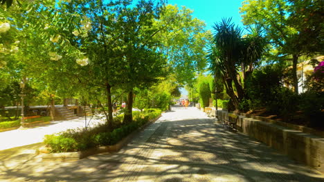 Sunny-path-in-a-lush-park-with-blooming-flowers-and-greenery-in-Ronda,-Spain