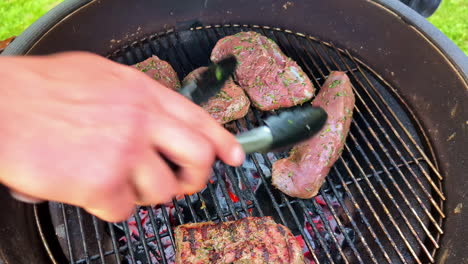 -A-close-up-view-of-seasoned-meat-being-grilled-over-hot-coals,-using-tongs-to-adjust-its-position