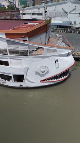 Saigon-River-cruise-boat-that-looks-like-a-fish-or-shark-in-vertical-video-orbit-from-front-to-side-at-the-Ho-Chi-Minh-City-port-on-sunny-clear-day.