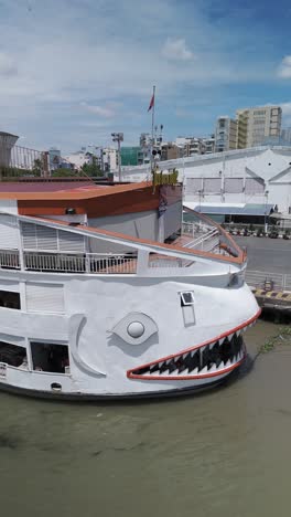 Saigon-River-cruise-boat-that-looks-like-a-fish-or-shark-in-vertical-video-orbit-from-front-to-side-at-the-Ho-Chi-Minh-City-port-on-sunny-clear-day