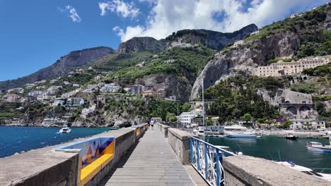 Walk-on-the-pier-at-Marina-Coppola-in-Amalfi-Harbor,-surrounded-by-the-Tyrrhenian-Sea,-the-Gulf-of-Salerno,-majestic-mountains,-lush-vegetation,-and-boats-in-Italy