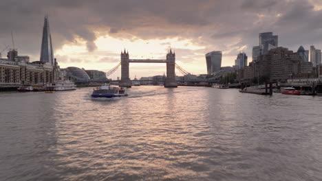 Niedrige-Drohne-Dolly-Vorbei-An-Der-Fähre-Auf-Der-Themse-In-Richtung-London-Tower-Bridge-Bei-Sonnenuntergang