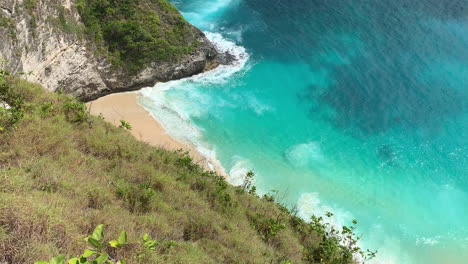 Overhead-panning-shot-of-turquoise-water-and-white-sand-revealing-rocky-cliff-of-Kelingking-Beach-in-Nusa-Penida,-Bali,-Indonesia