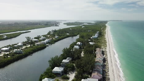 High-and-wide-shot-with-camera-tilting-down-white-drone-is-rising-to-showing-private-beach-community-with-beautiful-aqua-teal-blue-shoreline-and-waves