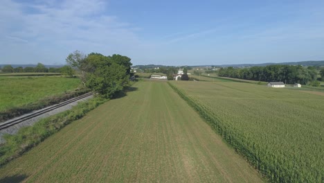 Aerial-View-Close-up-of-Green-Agricultural-Farm-Lands-Next-to-a-Rail-Road-Track-in-Amish-Countryside-on-a-Sunny-Summer-Day