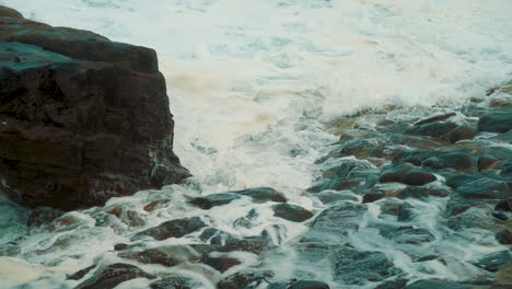 Ocean-white-wash-and-waves-slowly-crashing-over-rocks-and-stones-in-cornwall,-england,-120fps-slow-slow-motion