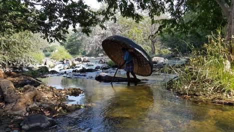 Un-Hombre-Cruzando-Un-Arroyo-Del-Río-Cauvery-Llevando-Un-Coracle-Y-Un-Remo-En-Hogenakkal,-Tamilnadu,-India