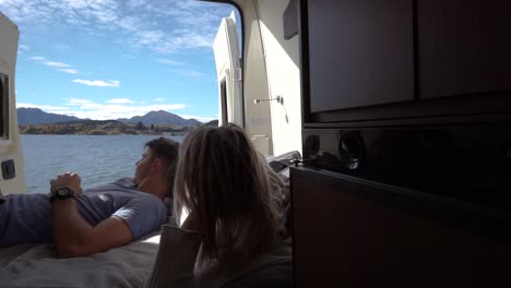 Slowmo---Young-couple-lying-in-back-of-campervan-and-looking-at-Lake-Wanaka,-New-Zealand