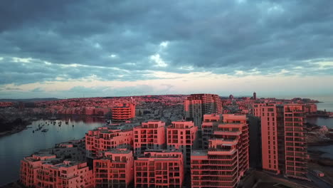 Drone-shot-of-the-red-morning-light-on-a-clowdy-day-reflecting-harmoniously-on-apartment-buildings-in-Sliema,-a-city-in-Malta