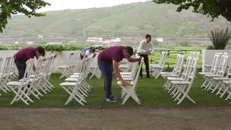 Group-of-people-cleaning-wet-chairs-arranged-in-garden-for-a-wedding-ceremony-in-Quinta-da-Pacheca,-Lamego,-Viseu,-Portugal