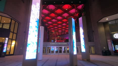 Editorial,-view-of-entrance-hall,-doorway-of-a-shopping-center,-colorful-digital-screens,-modern-architecture-and-red-lights-in-the-ceiling-and-people,-clients-passing-and-entering-the-mall