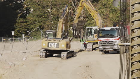 Excavator-working-on-a-construction-site-in-Vienna,-Austria-digging-dirt-and-unloading-it-into-a-truck