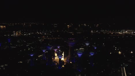 Flyinge-closer-onto-giant-mushroom-konstruktion-at-gardens-by-the-Bay-Singapore-at-night,-when-lights-shining-and-glowing---aerial-drone-shot