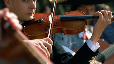 Un-Hombre-En-Una-Banda-De-Mariachi-Tocando-El-Violín-Mientras-Sus-Compañeros-Tocan-La-Guitarra-Y-Otros-Instrumentos-Para-Entretener-A-La-Multitud-Mirando