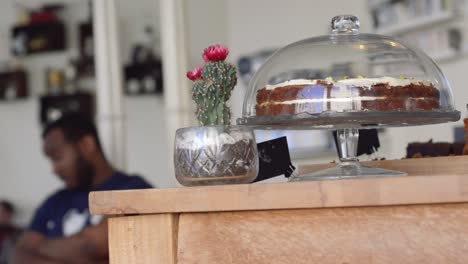 A-blurred-shot-of-friends-talking-in-a-cafe,-with-a-cake-in-a-glass-dome-in-the-foreground-|-Gourmet-Coffee-House-|-Shot-in-HD-at-cinematic-24-fps