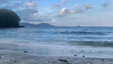 Boom-down-shot-revealing-trash-as-beautiful-blue-waves-wash-ashore-Blue-Lagoon-Beach-in-Bali,-Indonesia