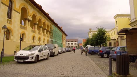 Toma-Panorámica-Caminando-De-Personas-En-Bicicleta-Frente-A-Un-Edificio-En-Alba-Iulia-Rumania