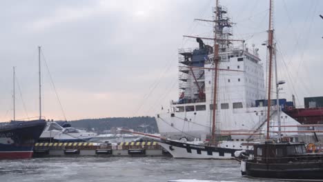 Big-cargo-ship-and-boats-parked-and-stuck-in-frozen-waters-of-industrial-port-in-winter-on-calm-overcast-day