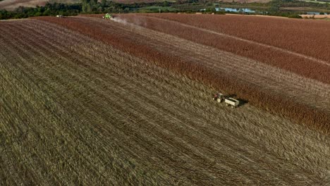 Vista-Aérea-Siguiendo-El-Tractor-Y-El-Remolque-En-El-Campo-De-Girasol-Búlgaro-Cosechando-Semillas-A-Principios-De-La-Noche-Del-Verano.