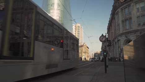 Metrolink-Tram,-car-and-bus-passing-by-to-REVEAL-National-Football-Museum-in-Manchester,-UK