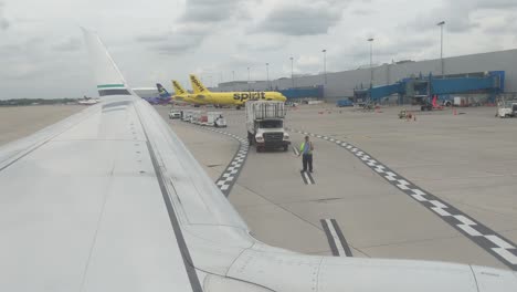 Looking-out-the-window-over-the-wing-of-an-airplane-as-it-rolls-back-to-prepare-for-take-off,-Detroit-Metro,-DTW,-cloudy