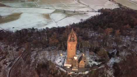 Aerial-orbital-shot-of-William-Wallace-Monument-in-Stirling,-Scotland,-during-blue-hour-on-a-cold-winter-evening