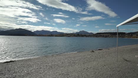 Young-couple-sitting-outside-at-campervan-on-beach-by-Lake-Wanaka,-New-Zealand