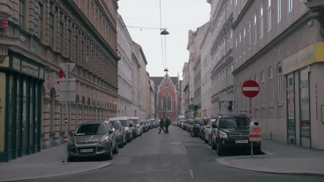 Crossroads-with-many-vehicles-and-cars-passing-by,-in-the-middle-of-Vienna,-Austria,-near-houses-and-buildings,-with-a-cathedral-in-the-background,-on-a-cloudy-day