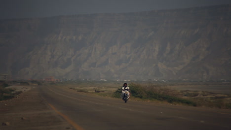 Una-Vista-En-Perspectiva-De-Una-Carretera-Vacía-Con-Enormes-Montañas,-Un-único-Ciclista-Avanza