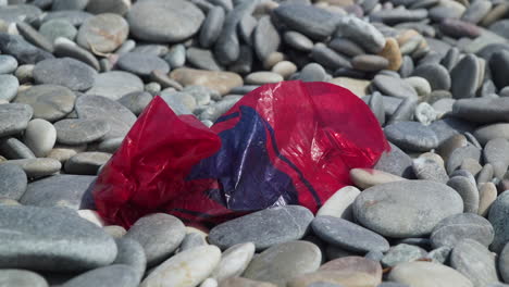 Red-plastic-bag-littering-a-pebble-beach-slow-zoom-out