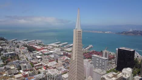 Aerail-view-of-trans-america-tower-with-ocean-and-treasure-island-in-background-on-a-cloudy-day-in-san-francisco-downtown-drone-footage-and-urban-houses-below
