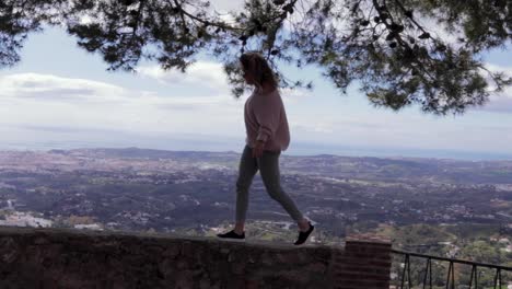 Beautiful-woman-walks-across-wall-with-a-view-over-Spain-in-the-background