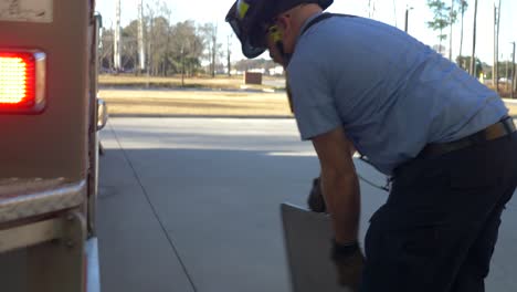 Firefighter-walks-around-firetruck-with-emergency-lights-flashing-in-the-morning