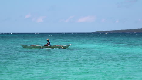 A-local-fisherman-paddles-his-boat-in-the-ocean-of-Boracay,-Philippines