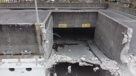 Descent-of-a-drone-closely-facing-a-old-demolished-parking-garage-with-local-gardens-in-the-back-of-building