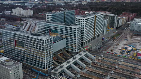Aerial,-tilt,-drone-shot-towards-the-Mall-of-Tripla-shopping-center-and-the-Pasila-railway-station,-on-a-partly-sunny-evening,-in-Helsinki,-Finland