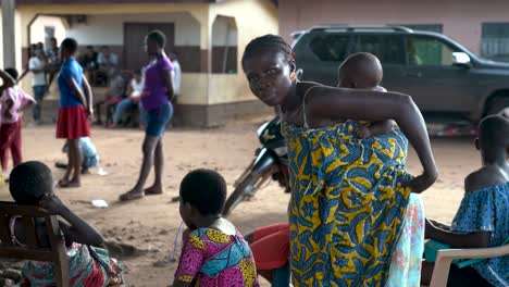 A-woman-with-a-baby-on-her-back-wraps-colorful-Kent-cloth-around-her-and-her-baby-to-create-a-traditional-baby-carrier