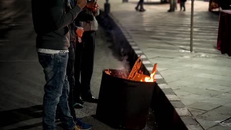 Menschen,-Die-Sich-An-Einem-Kalten-Abend-Vor-Einem-Feuer-Wärmen,-Das-In-Der-Nähe-Der-Straße-Angezündet-Wird