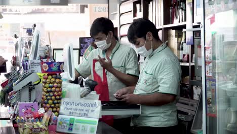 Shot-of-Two-Seven-Eleven-Workers-Counting-Money-and-Wearing-Face-Mask-Due-to-Coronavirus-Outbreak-In-Bangkok-Thailand