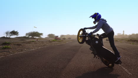 Close-shot-of-a-motorcycle-stunt-rider-doing-wheelie-tricks-on-the-road-at-sunset