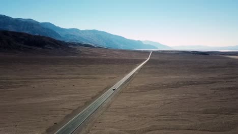 Ein-Drohnenschuss-Eines-Autos-Auf-Der-Autobahn-In-Richtung-Horizont-In-Einer-Death-Valley-Wüste-In-Kalifornien