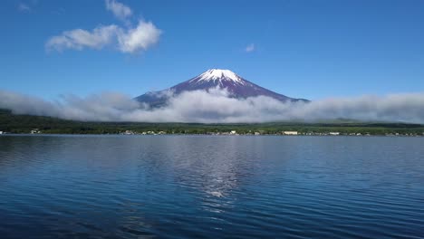 Mount-Fuji-with-low-laying-clouds-and-fog,-stunning-aerial-fly-over-lake-Kawaguchi