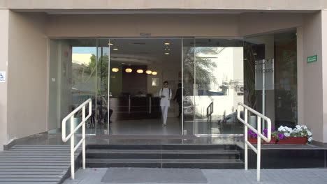 Alkindi-Specialised-Hospital's-main-entrance-with-nurse-exiting-the-building-while-looking-at-her-mobile-phone