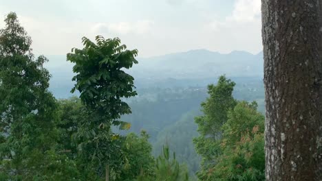 Looking-over-the-hills-and-nature-scenery-on-a-cloudy-day-with-the-sun-breaking-through-in-Bandung,-Indonesia-on-top-of-a-cliff